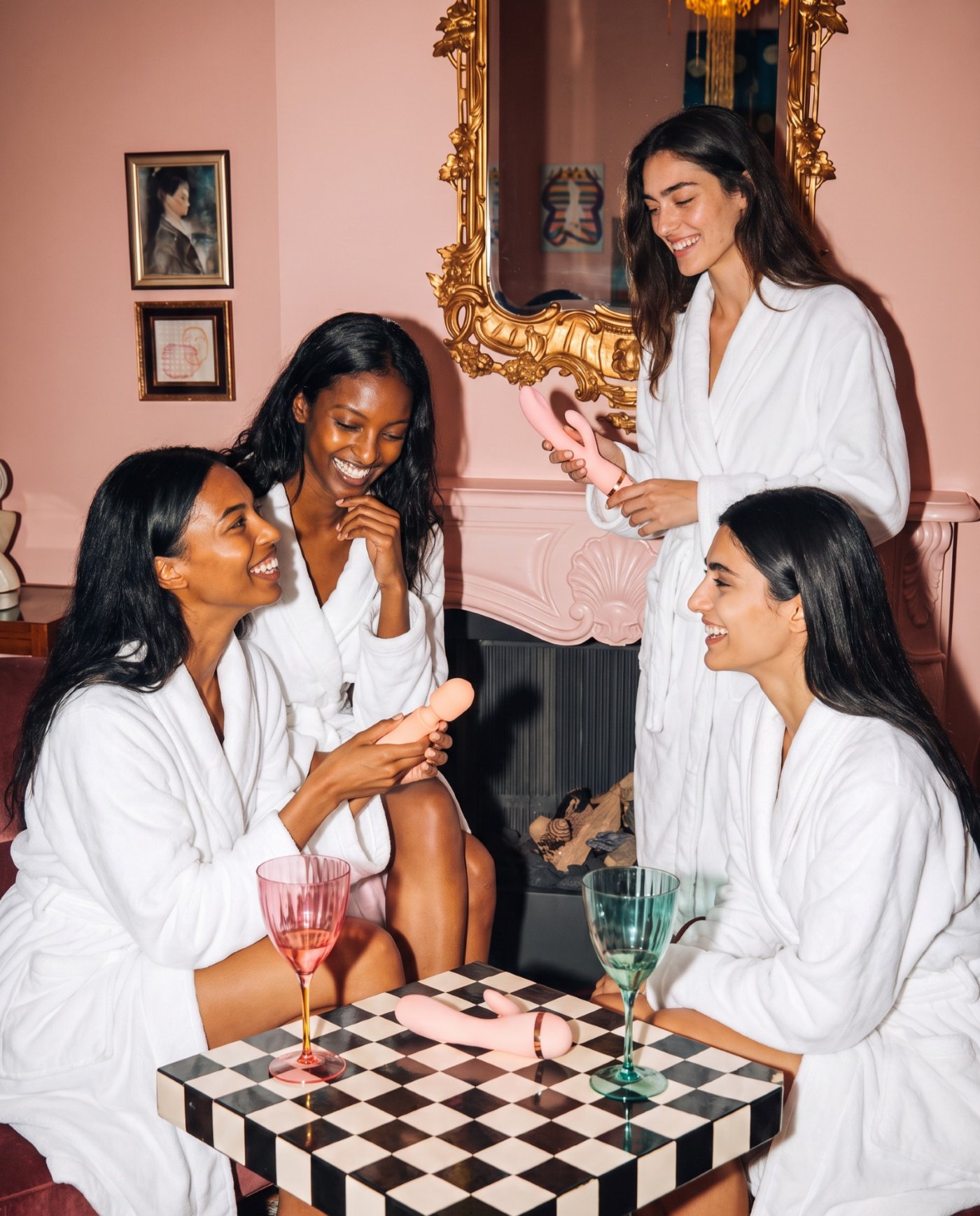 Four friends in white robes laughing together in a pink sitting room, VUSH pieces on the table between them